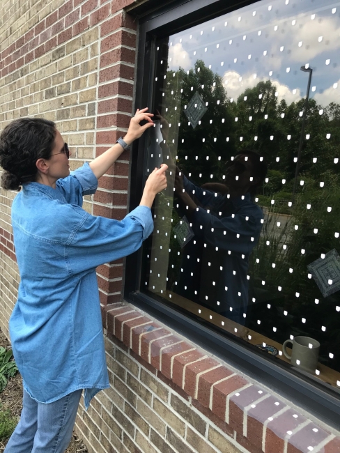 Woman applying closely spaced white dot markers to the outside of a reflective window.